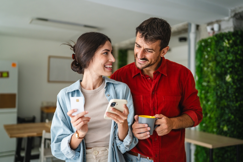 Femeie care ține într-o mână un card și în cealaltă telefonul, alături de un coleg de birou