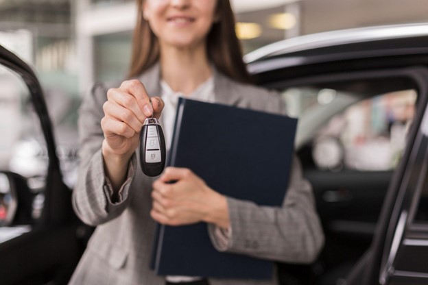 Femeie imbracata business care intinde cheia unui automobil